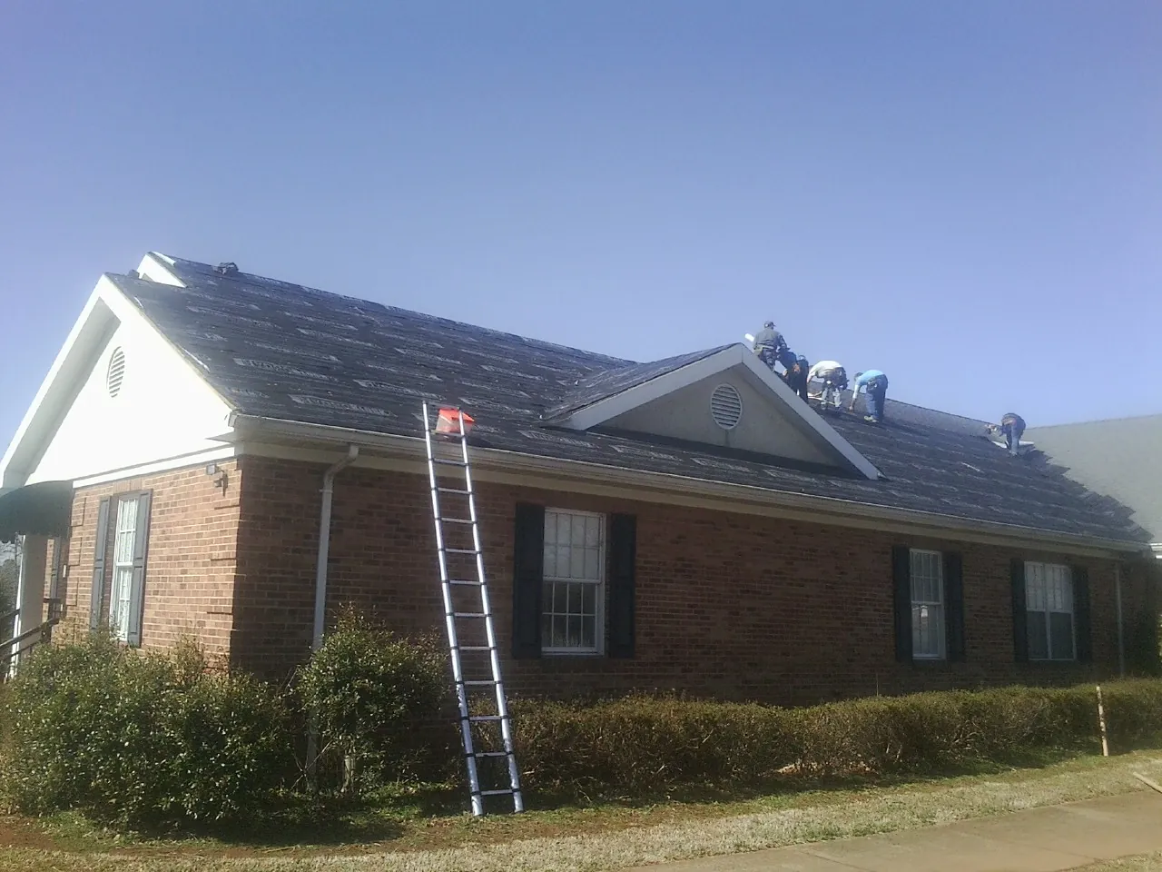 Crew tearing shingles off a brick ranch roof with a ladder set — Emergency Roof Repair work by our crew in Norwich