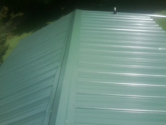 New green metal panels meeting at the ridge of a roof — Flat Roof Repair work by our crew in Norwich
