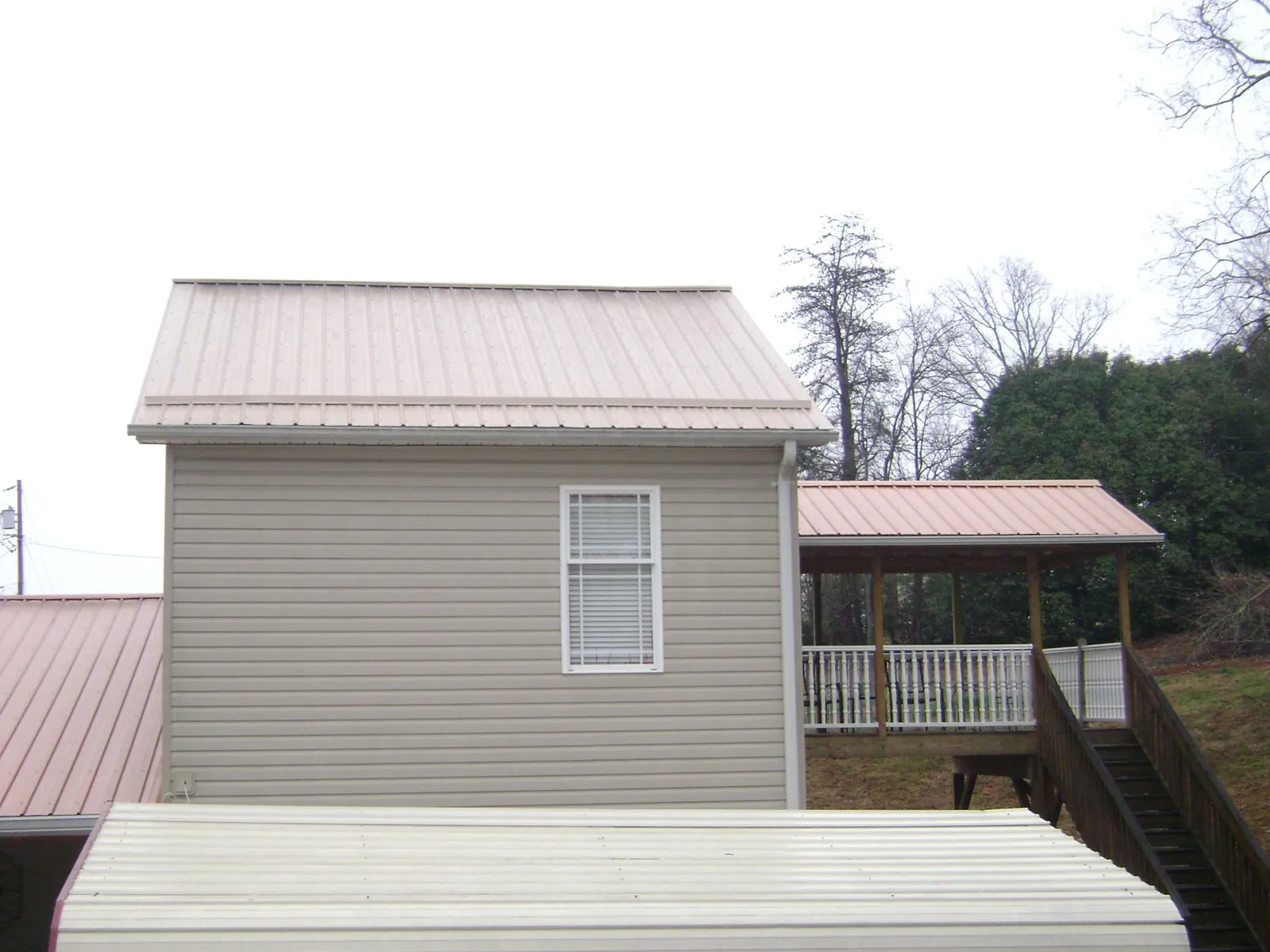 Tan metal roofs on a two story addition and attached porch, from a Roof Replacement job in Norwich
